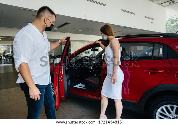 Young couple in masks
selects a new vehicle and consult with a representative of the
dealership in the period of the pandemic. Car sales, and life
during the pandemic