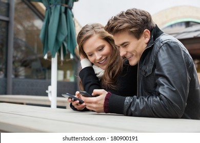 Young Couple Messaging Through Mobile Phone While Leaning On Bench