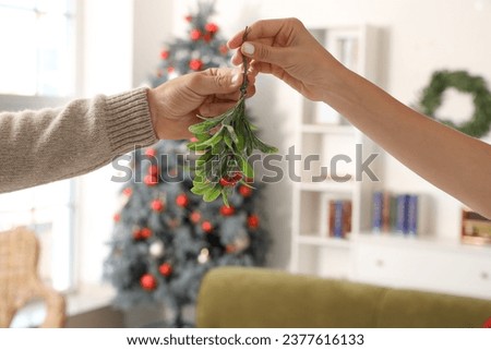 Young couple with mistletoe branch at home on Christmas eve, closeup