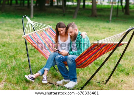 Young couple with mobile phone sitting on hammock