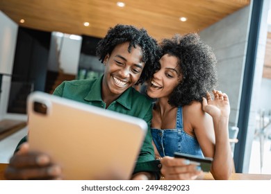 Young couple in a modern living room in a cheerful and connected atmosphere, looking at tablet, shopping online using a credit card. Smiling and enjoying their time excited about purchase - Powered by Shutterstock