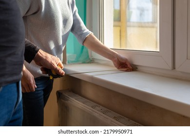 Young couple moving in new apartmen. People measure size of window sill with a tape measure. Concept new homes, new beginning. High quality photo