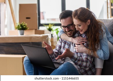 Young couple moving in new home. Sitting and relaxing after unpacking. Searching home decorating ideas on laptop