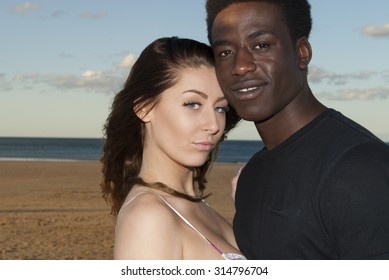 Young couple multicultural head and shoulders heads together looking  into camera on beach  romantic emotions