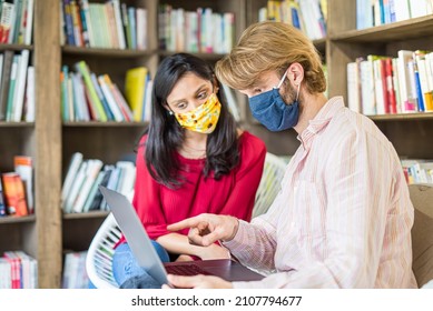 young couple of multiracial students using laptop in a library during Corona Virus epidemic, wearing face mask fro protection, team work and health care concepts - Powered by Shutterstock