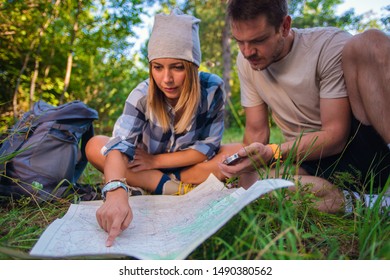Young couple navigasting using map and compass inside the forest. Hiking concept in the mountain in summer