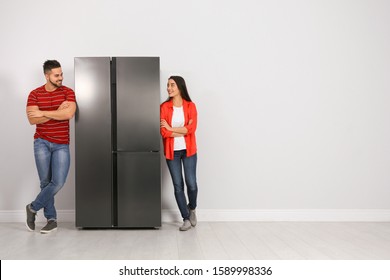 Young couple near refrigerator indoors, space for text