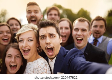 Young couple of newlyweds with group of their firends taking selfie and making funny grimaces - Shutterstock ID 220447822