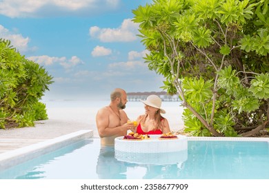 young couple newlyweds spend time together in honeymoon admiring in swimming pool with served floating tray drinks and snacks on tropical island resort in Maldives, breakfast for romantic date, luxury