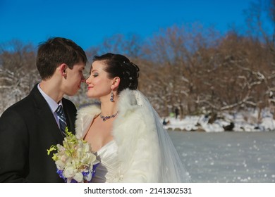Young couple newlyweds walking in a winter forest in the snow. Bride and groom hugging in the park in winter. Beautiful man and woman in their wedding clothes are among the pines.