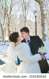 Young couple newlyweds walking in a winter forest in the snow. Bride and groom hugging in the park in winter. Beautiful man and woman in their wedding clothes are among the pines.