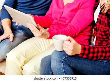 Young Couple With Old Woman Sitting On Couch And Watching Something On Tablet
