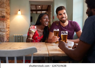 Young Couple And An Older Man Drinking At A Table In A Pub