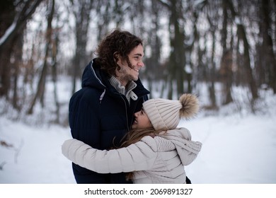 Young couple on a date outdoors in the forest in winter. Short woman hugging her tall boyfriend.