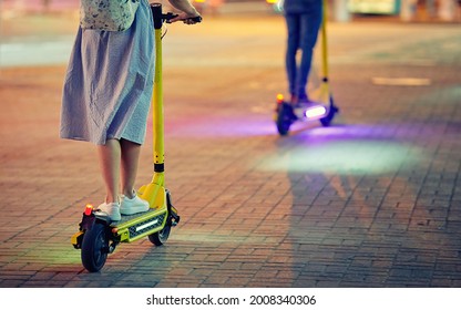 Young couple on electric scooter with  headlights drive through  city street at night. E-scooter or motorized vehicle for walking around. Woman riding on electric scooter. Urban transportation - Powered by Shutterstock