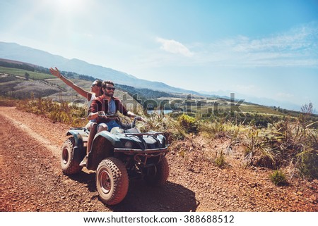 Young couple on an off road adventure. Man driving quad bike with girlfriend sitting behind and enjoying the ride in nature.