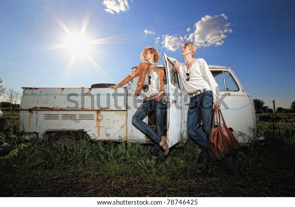 A young couple on a old broken car in a field\
man is holding a leather bag