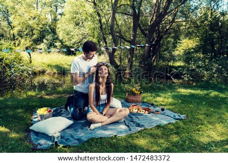 Young couple on a picnic sitting on a blanket The man put on her head flower crown Selective focus 