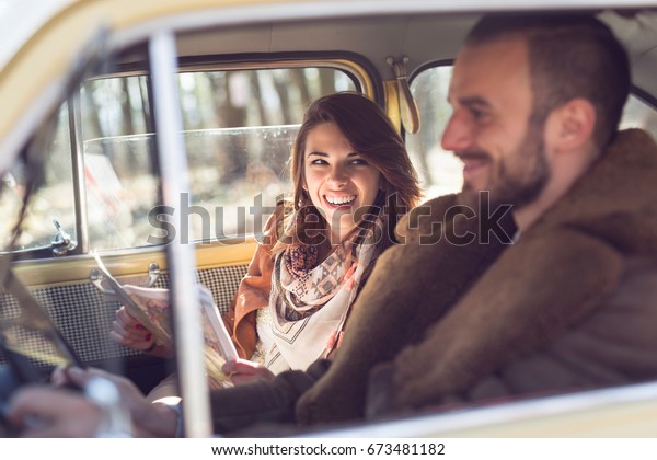 Young couple\
on a road trip, enjoying the sunny day and having fun, girl reading\
the map while guy is driving a\
car