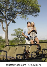 Young Couple On Safari Standing In Jeep And With Binoculars