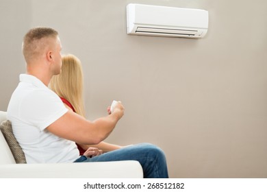 Young Couple On Sofa Using Air Conditioner