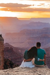Young Couple On A Steep Cliff Taking In The Amazing View Over Famous Grand Canyon On Beautiful Sunset In Summer, Grand Canyon National Park, Arizona. High Quality Photo