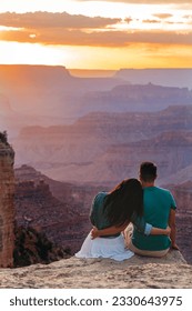 Young couple on a steep cliff taking in the amazing view over famous Grand Canyon on beautiful sunset in summer, Grand Canyon National Park, Arizona. High quality photo