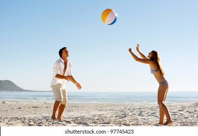 Young Couple On A Summer Beach Vacation Playing With A Beachball And Having Carefree Fun