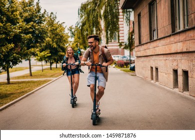Young couple on vacation having fun driving electric scooter through the city.