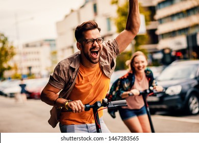 Young couple on vacation having fun driving electric scooter through the city.	