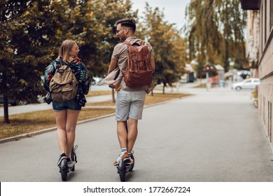 Young Couple On Vacation Having Fun Driving Electric Scooter Through The City.