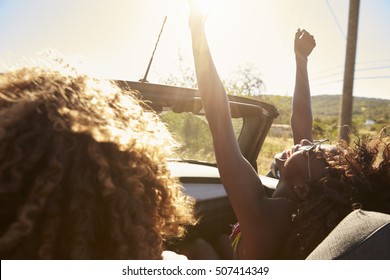 Young couple in an open top car, woman with arms raised - Powered by Shutterstock