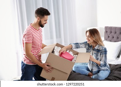 Young Couple Opening Parcel In Bedroom At Home