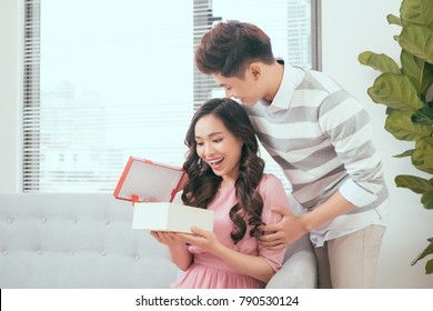 Young Couple Opening Parcel Gift Box On The Couch