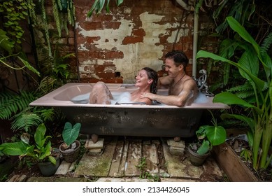 A young couple in an outdoor foam bath. She has her eyes closed and is smiling while he massages her shoulders. 