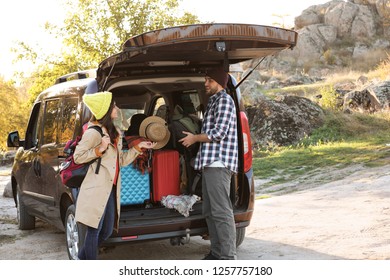 Young Couple Packing Camping Equipment Into Car Trunk Outdoors. Space For Text