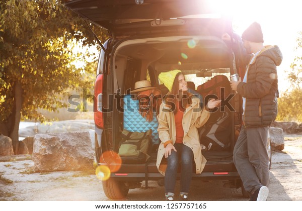 Young couple packing camping equipment into car\
trunk outdoors. Space for\
text