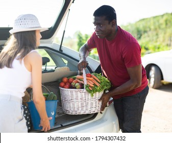 Young couple packing harvested vegetables and greens in car trunk