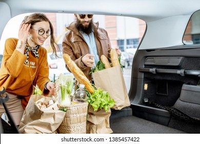 Young Couple Packing Shopping Bags With Fresh Food Into The Car Trunk, View From The Vehicle Interior