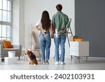 Young couple with paint rollers and Beagle dog during repair in their new house, back view