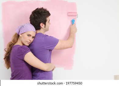 Young Couple Painting Baby Nursery In New Home Pink