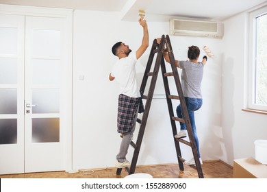 Young Couple Painting Indoor Walls In Their New Home