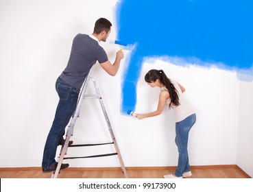 Young Couple Painting Wall At Home In Blue