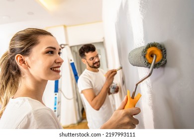 Young Couple Painting Wall In Their Home.