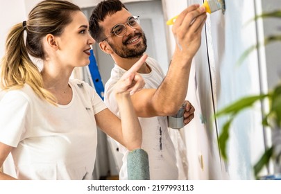 Young Couple Painting Wall In Their Home.