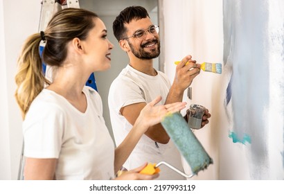 Young Couple Painting Wall In Their Home.