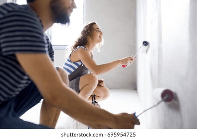 Young Couple Painting Walls In Their New House.