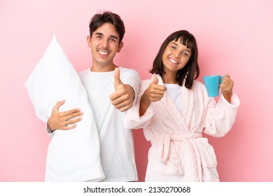 Young couple in pajamas isolated on pink background giving a thumbs up gesture because something good has happened