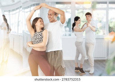 Young couple performs an expressive salsa in bright, modern dance studio during a group class