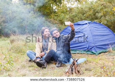 Young couple are photographed at the phone in autumn forest.